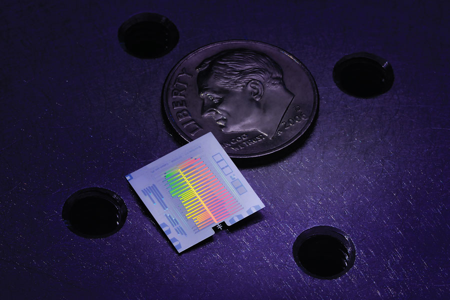
       A prototype single-chip spectrometer operating in the millimeter-wave regime. The millimeter-wave signal is coupled from a waveguide (not shown) through a probe at the bottom of a chip and transmitted via superconducting microstrip down the center of the chip. Tuned filters along the microstrip redirect narrow bands of the radiation to individual detectors along the side of the microstrip to determine the spectral content of the original signal.
    